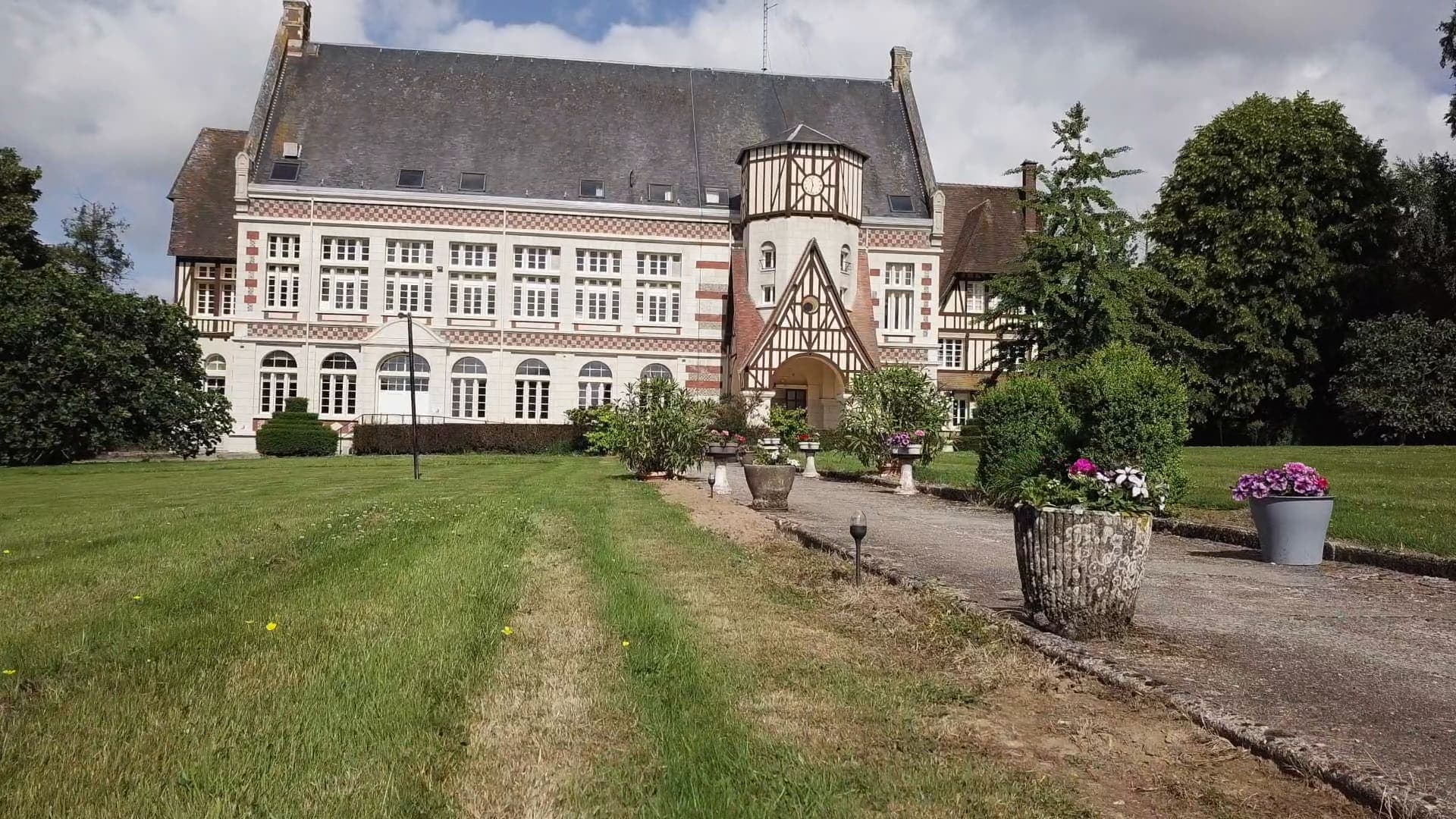 L’allée bordée de vasques fleuries qui mène à l’église, à travers la pelouse du parc.
