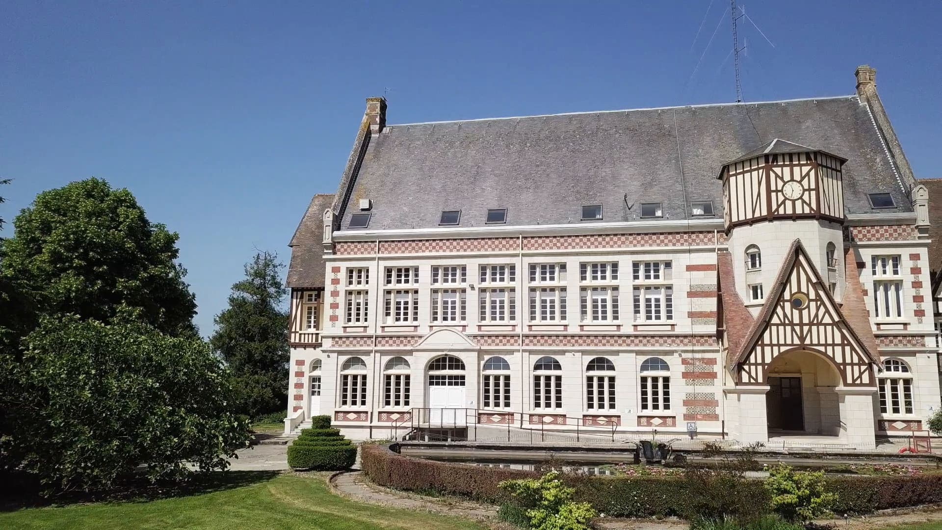 La façade de l’église côté jardin, sous un ciel bleu, au-dessus des massifs du bassin.